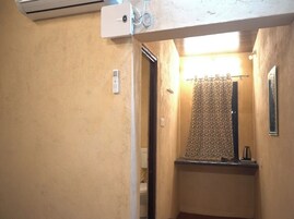 Un pasillo estrecho con un baño que incluye una cortina de ducha estampada, un lavamanos pequeño y un espejo.