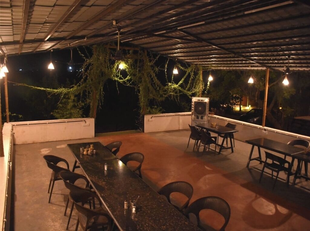 Un espace extérieur aménagé en terrasse, avec une longue table et des chaises, un haut-parleur et des guirlandes lumineuses.