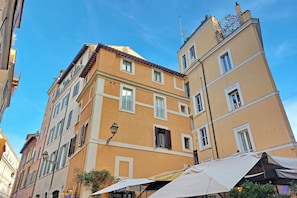 Um edifício de vários andares com fachada amarela, várias janelas e entrada visível no nível da rua.