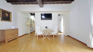 Een ruime kamer met houten vloeren, een eettafel met stoelen, een aan de muur bevestigde televisie en een houten kast.