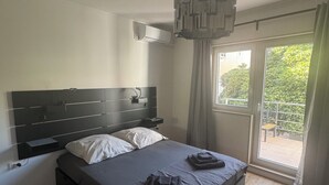 A modern bedroom with a large bed, a bedside table, a built-in air conditioning unit, and a view of the outdoors through a sliding glass door. - Two-bedroom House Lara Denona (Novalja)