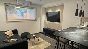 A modern living room with a sofa, a coffee table, a TV mounted on the wall, and a kitchen area with a marble countertop and bar stools. - Two-bedroom House Lara Denona (Novalja)