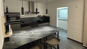 A modern kitchen with a marble countertop, two bar stools, a built-in oven, and pendant lights. - Two-bedroom House Lara Denona (Novalja)