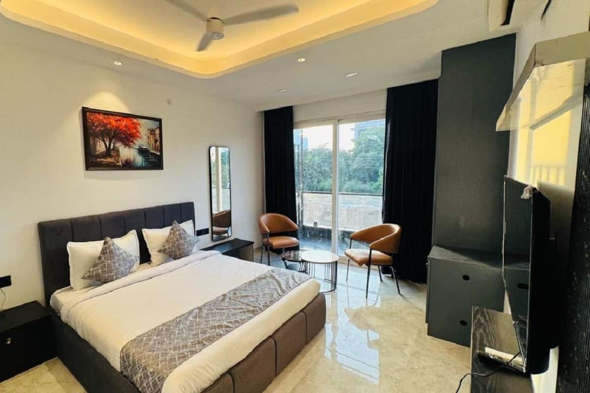 A modern hotel room with a large bed, a desk, two chairs, a TV, and a painting on the wall.
