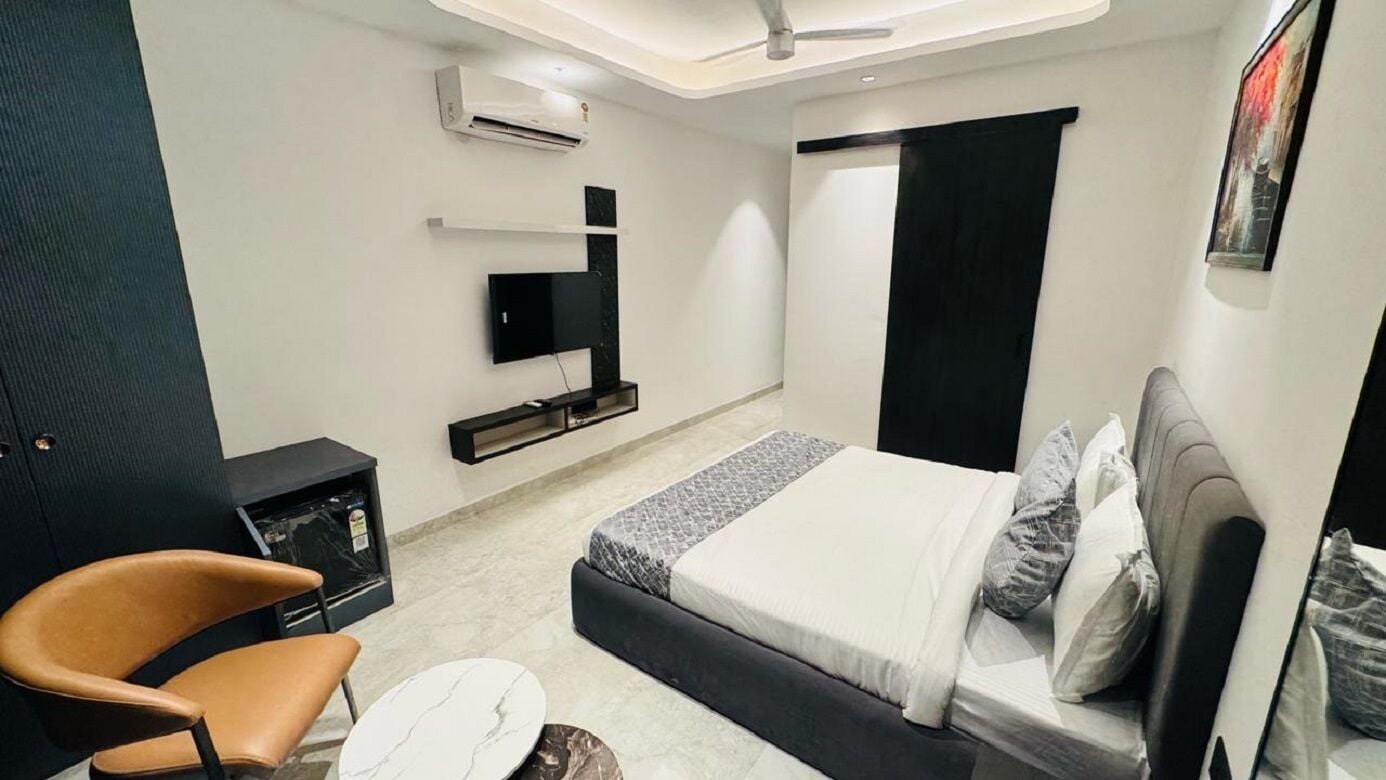 A modern bedroom with a bed, a chair, a small table, and a mounted TV.