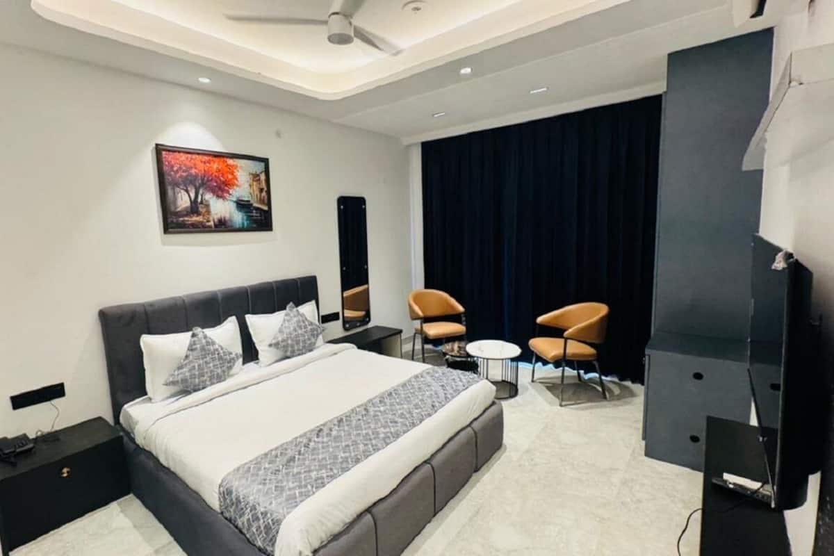 A modern hotel room with a large bed, a flat-screen TV, a ceiling fan, and a dark curtain backdrop.