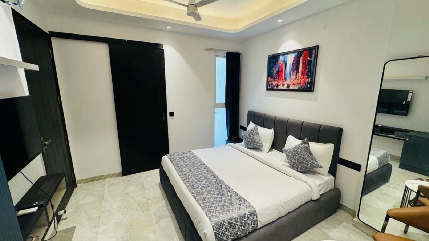 A modern bedroom with a large bed, a ceiling fan, a cityscape painting, and a TV on the wall.