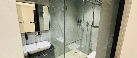 A modern bathroom with a glass-enclosed shower, a white sink, and a dark vanity.