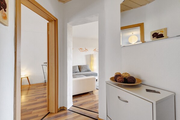 A room with a bed, a bedside table with a bowl of fruit, a mirror on the wall, and a wooden floor.