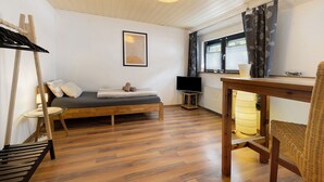 A room with a bed, a table, a chair, a television, and a window with curtains.
