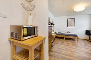 Une chambre moderne avec une table en bois, un four à micro-ondes, un lit, une télévision et un tableau encadré au mur.