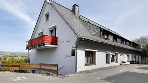 A two-story building with a sloped roof, a balcony with red railings, and a view of a town in the background.