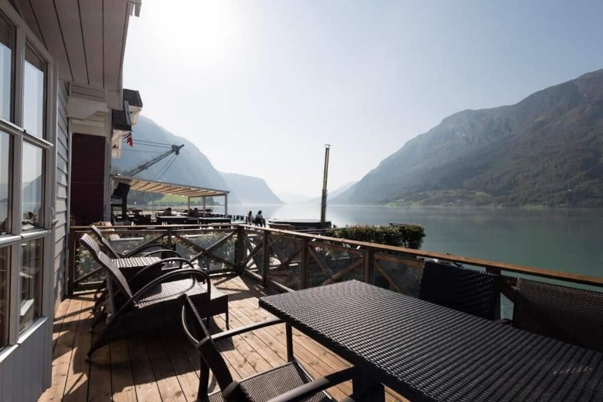 A wooden deck with outdoor seating, overlooking a lake and mountains.