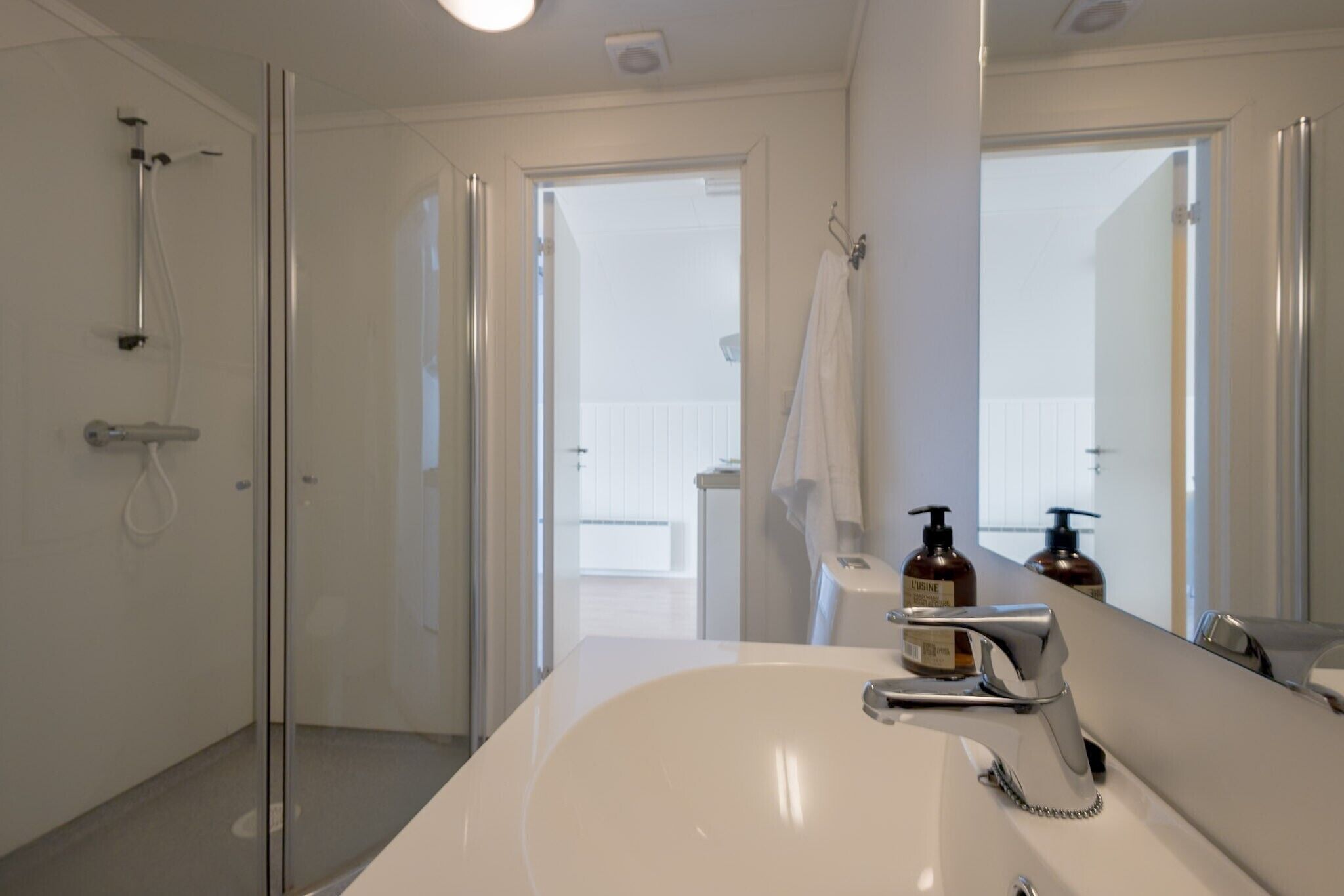 A modern bathroom with a large white sink, a glass-enclosed shower, and a view of a balcony through an open door.