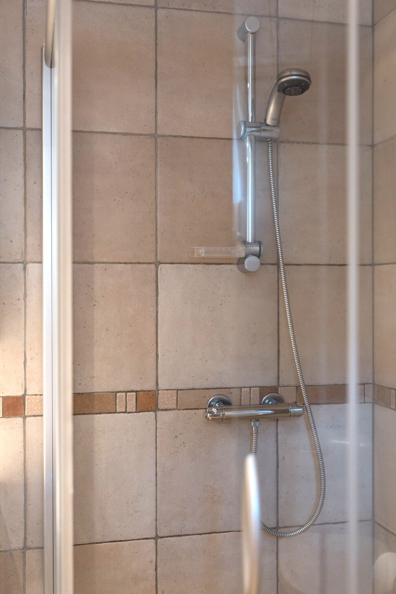 A shower with a handheld showerhead and a fixed showerhead, both mounted on a tiled wall.