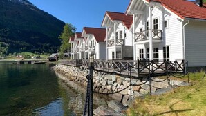 Una hilera de edificios blancos con techos rojos junto a un lago, con una montaña al fondo.