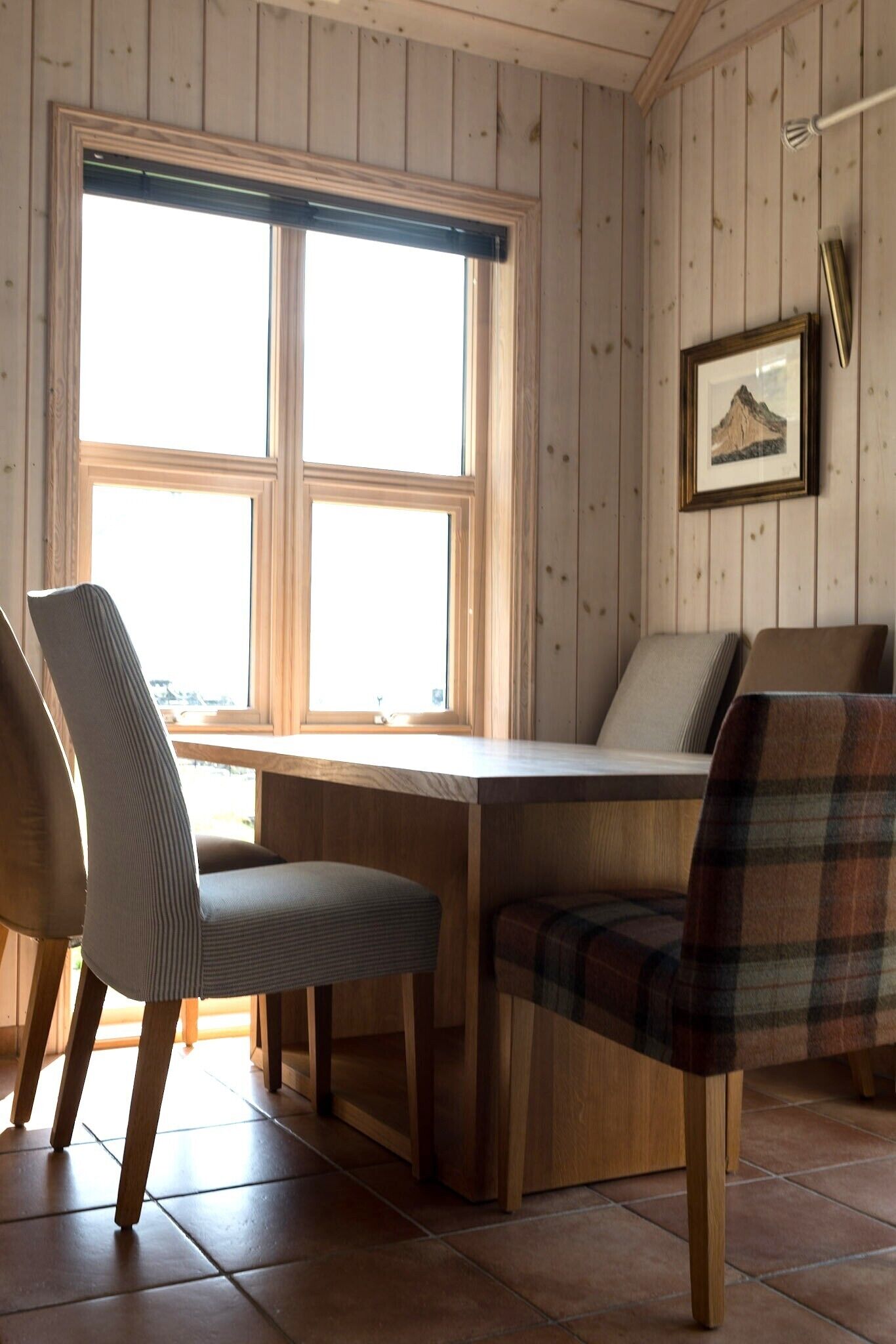 A wooden-paneled room with a large window, a table, and two chairs.