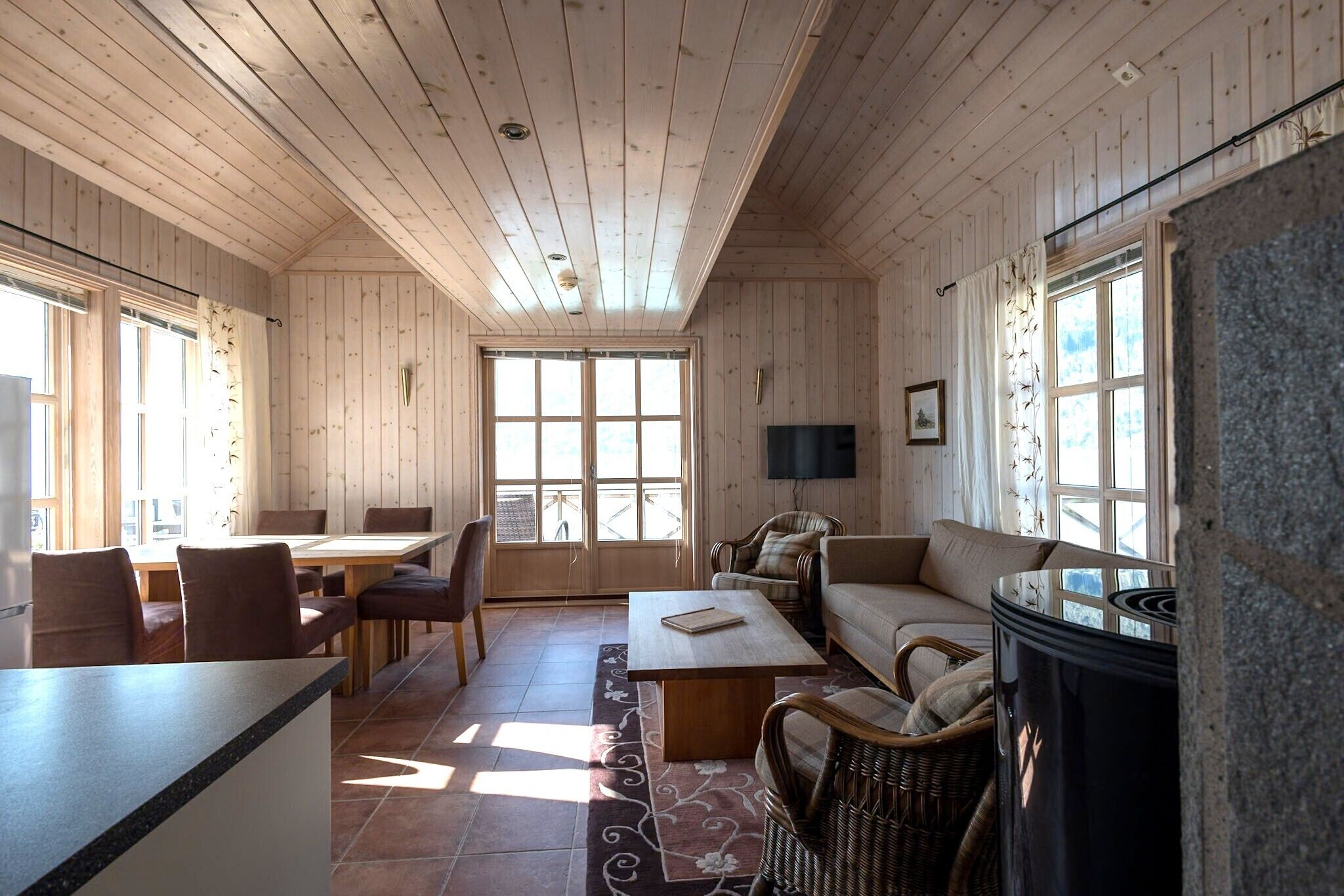 Interior de una cabaña de madera con comedor, sofá y chimenea.