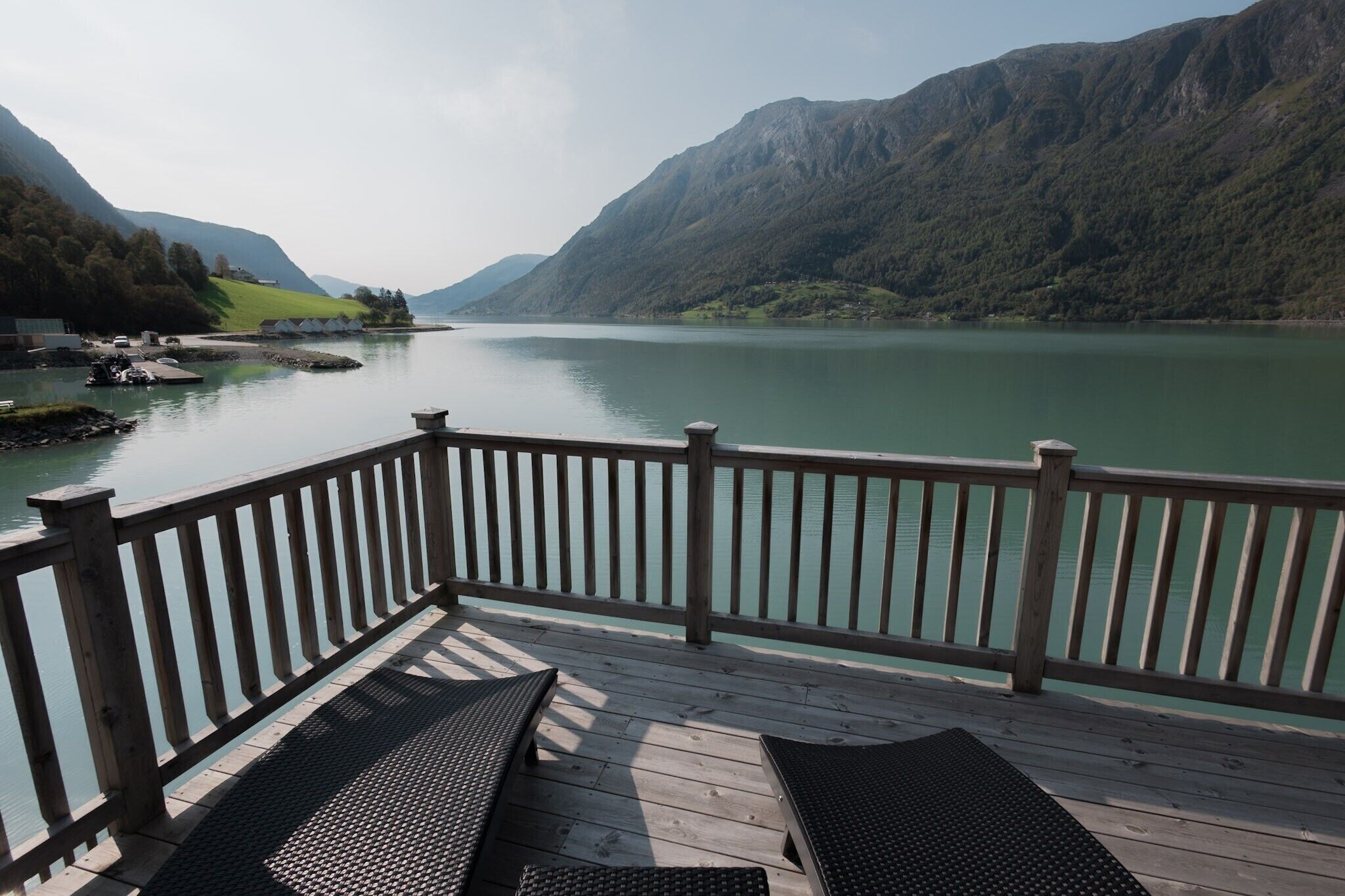 A wooden deck with two lounge chairs overlooking a calm lake, surrounded by mountains.
