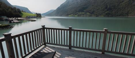 A wooden deck with two lounge chairs overlooking a calm lake, surrounded by mountains.