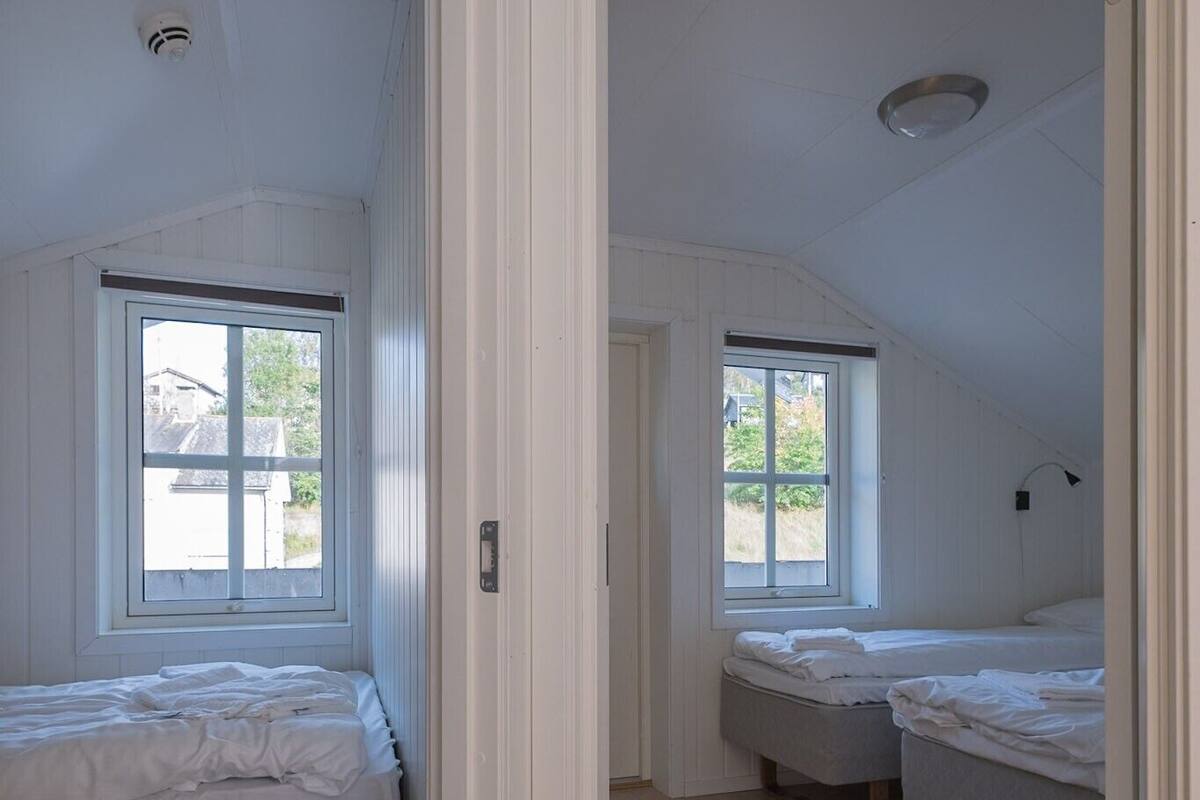 A room with two beds, wooden flooring, and a window with a view of greenery.