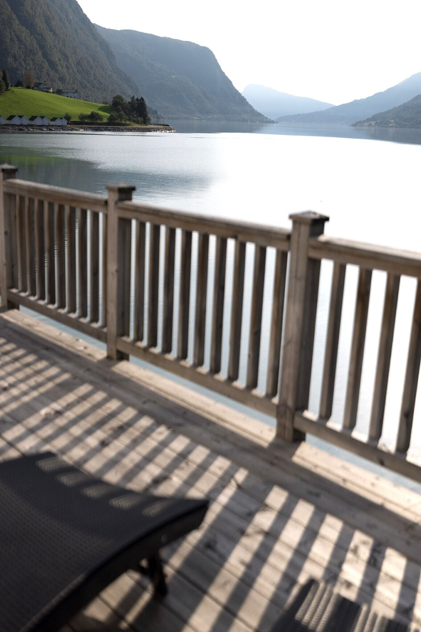Un molo in legno con ringhiera che si affaccia su un lago tranquillo, circondato da montagne.