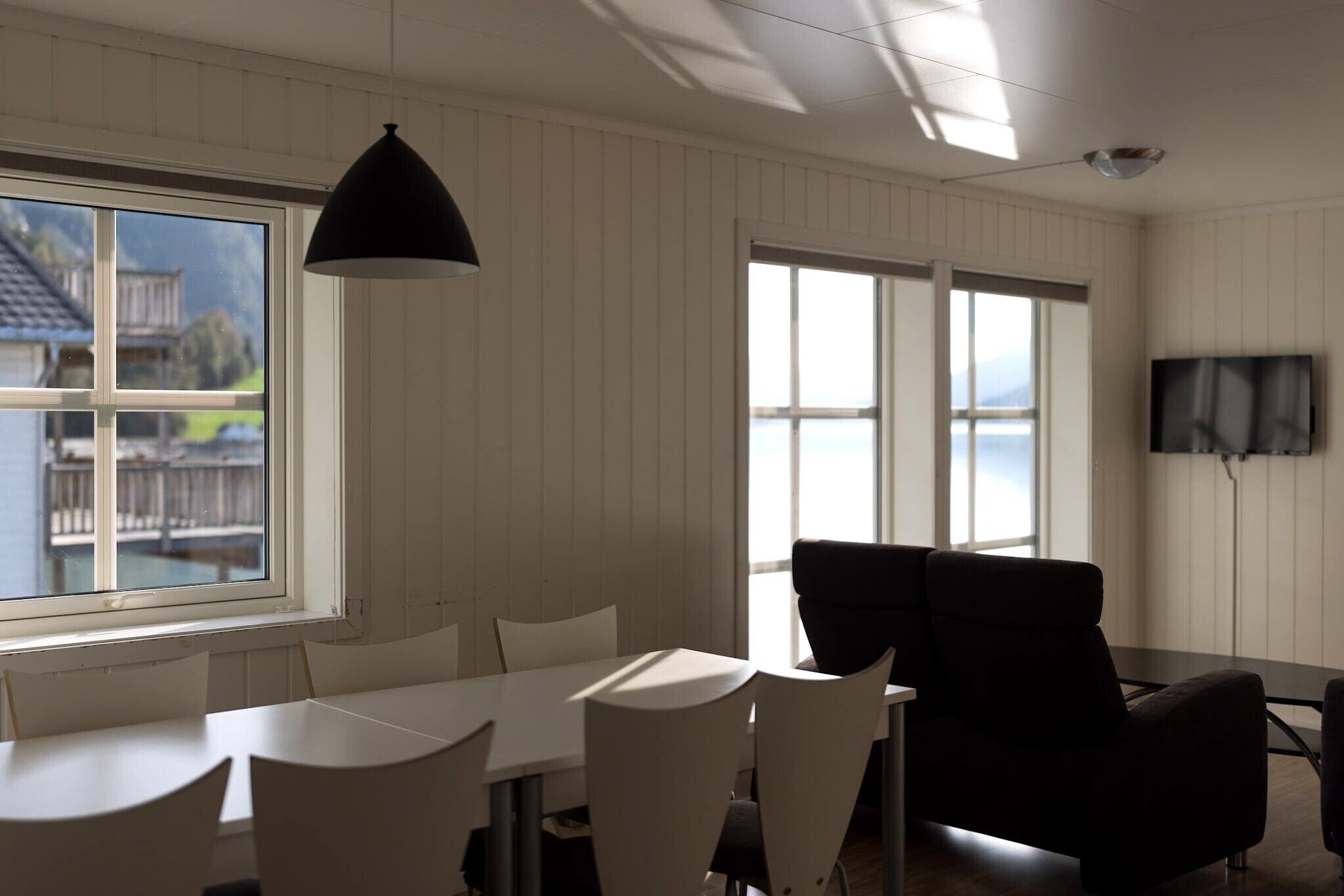 A dining area with a table and chairs, a black pendant light, and a TV mounted on the wall.
