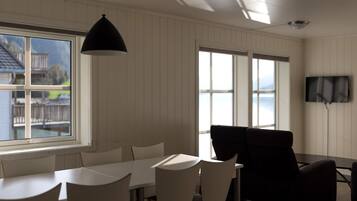 A dining area with a table and chairs, a black pendant light, and a TV mounted on the wall.