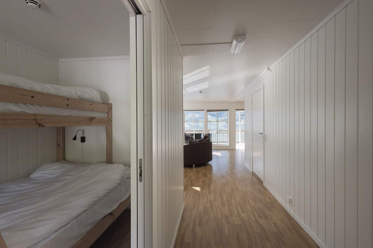 A room with a bunk bed, a sofa, and a view of the outdoors through large windows.