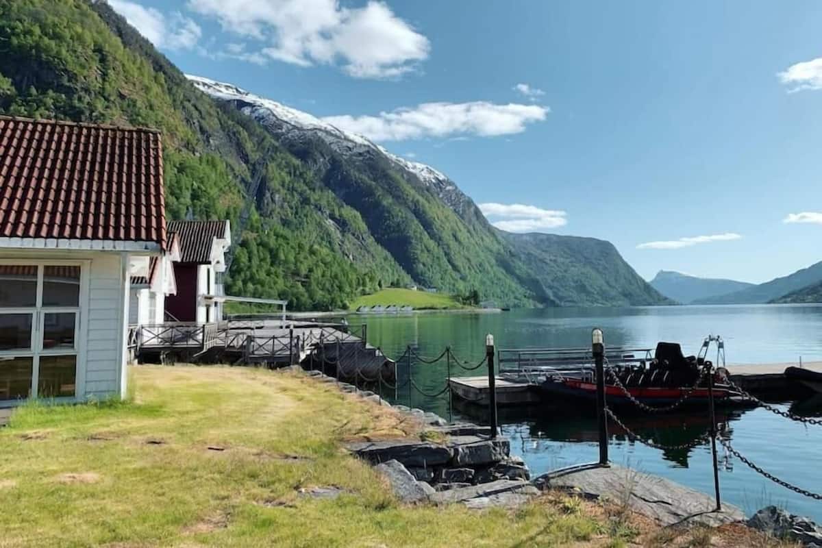 A lakeside cabin with a dock, surrounded by mountains and a clear sky.