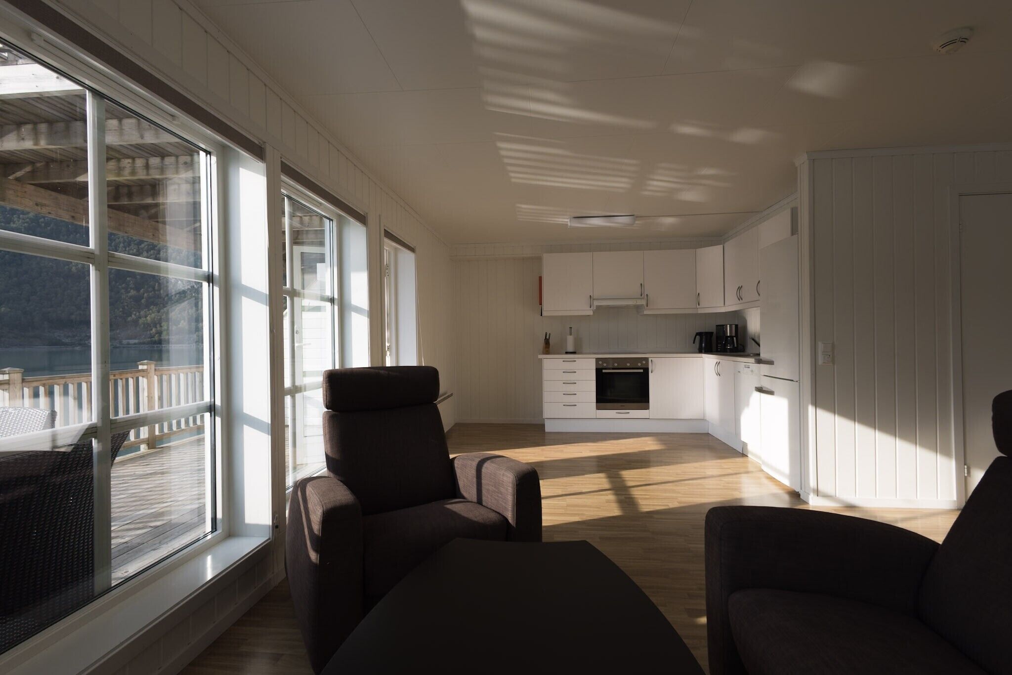 A spacious living area with a large window, a sofa, and a kitchen in the background.