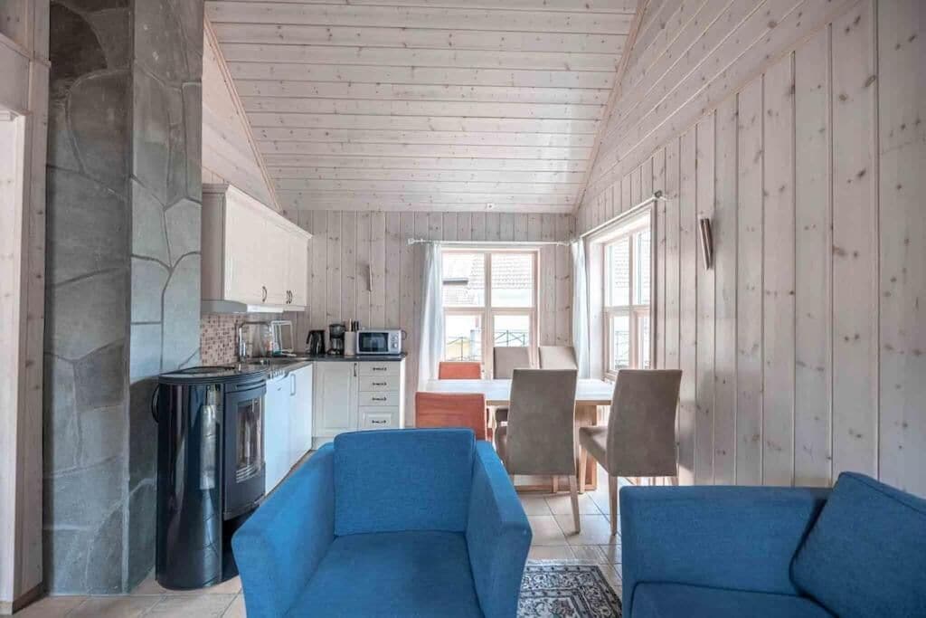 Un intérieur chaleureux avec une cheminée en pierre, des murs en bois et un coin repas comprenant des chaises et une table.