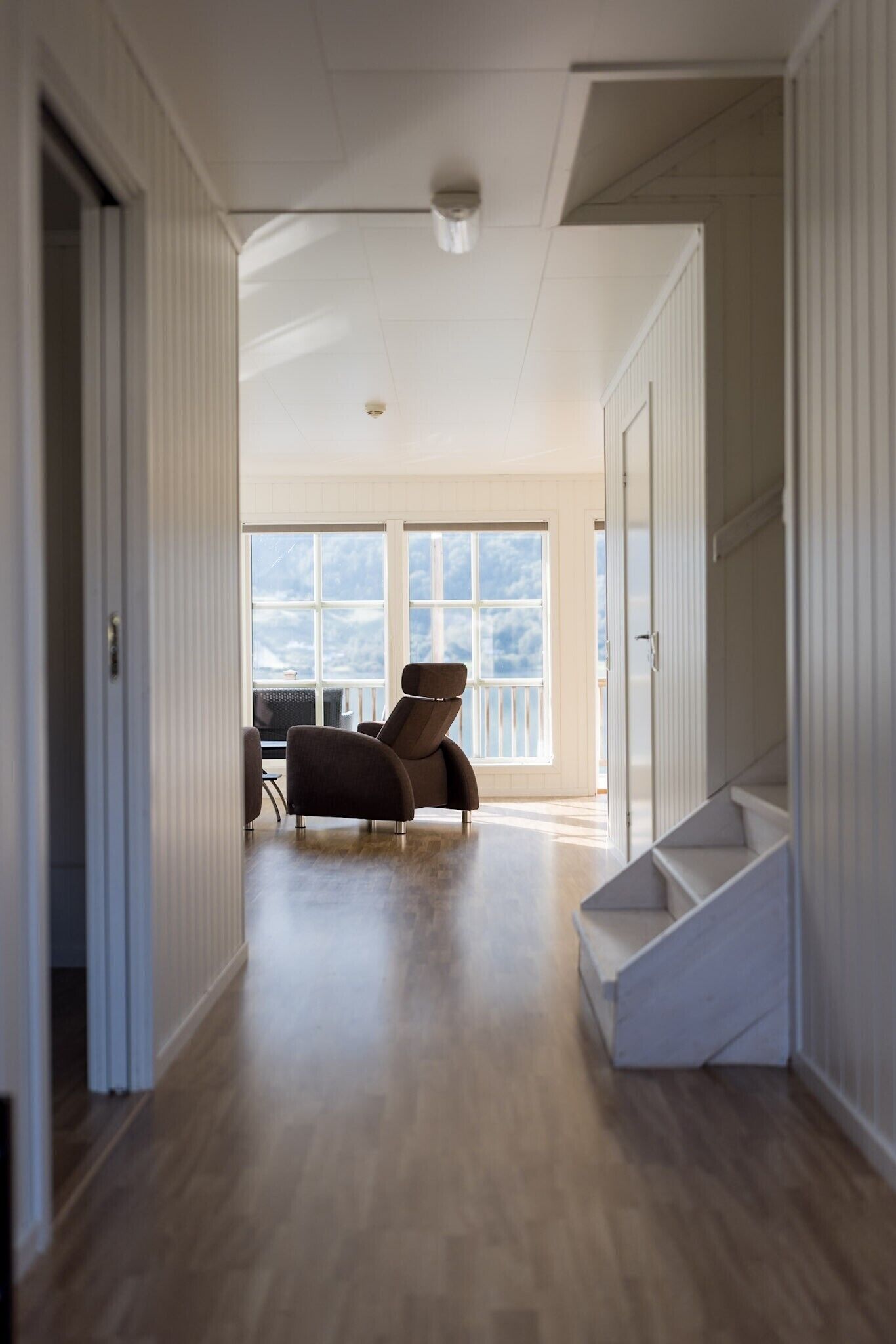 A hallway with a staircase, a seating area with a chair, and large windows.