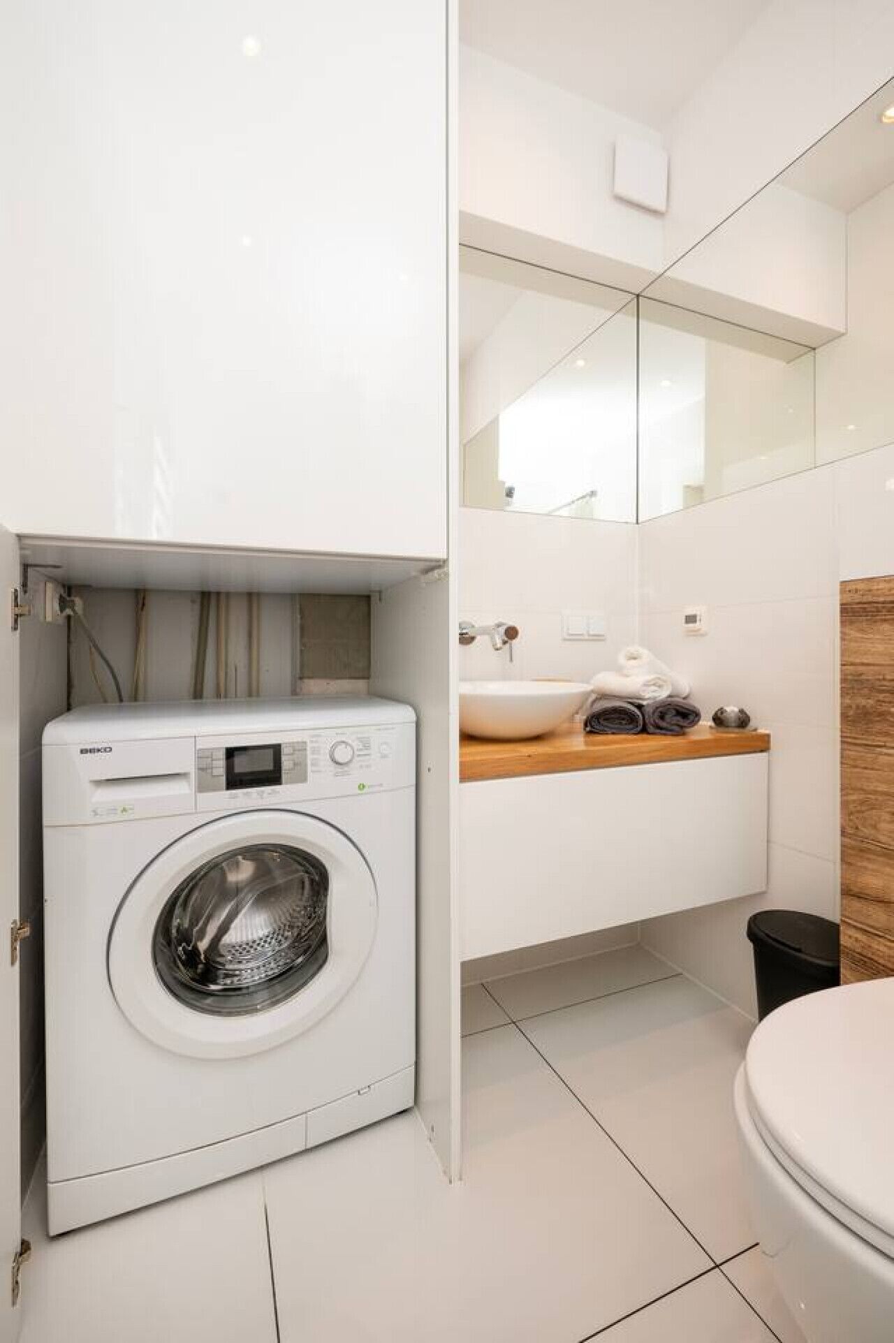 Un baño moderno y funcional con lavadora integrada, tocador de madera, lavabo e inodoro.