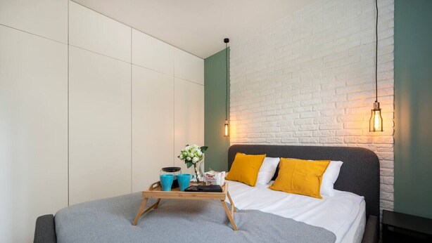 Een moderne slaapkamer met een bed, nachtkastje, wandlamp en een houten dienblad met spullen erop.