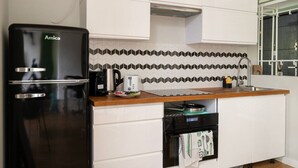 Een compacte keuken met witte kastjes, een zwarte Amica-koelkast, een gekleurde spatwand en een houten aanrecht.