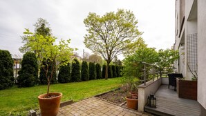 Een binnenplaats met een verhard terras, plantenpotten, een houten terras en een klein zitgedeelte.