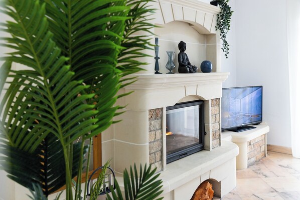 A living room with a fireplace, a television, and various decorative items. - Primula e Foca (St. Julian's)