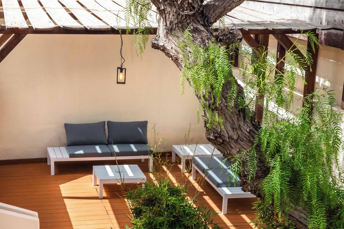 Une terrasse en bois avec des sièges d’extérieur, un mur en pierre et un arbre.