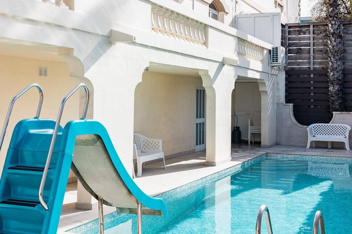 Un espace piscine avec un toboggan, des chaises blanches et une clôture en bois.