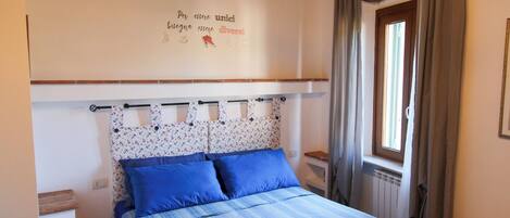 Quarto com cama, almofadas azuis, colcha listrada e uma parede com uma frase motivacional.