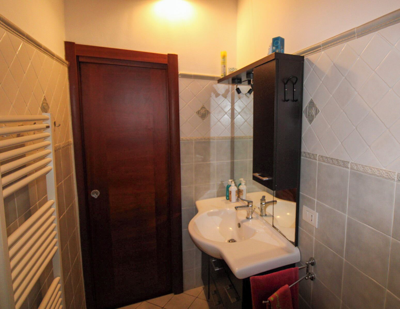 A bathroom with a wooden door, a white sink, a mirror, and a towel rack.