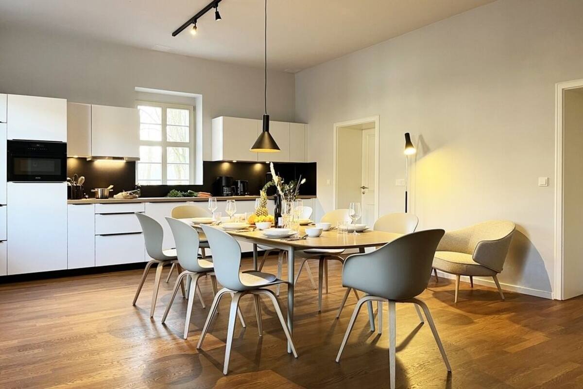 A modern kitchen with white cabinets, a dining table with chairs, and a pendant light.