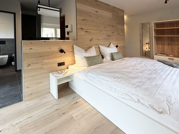 A modern bedroom with a wooden headboard, a white bed, and a nightstand with a lamp. - Resort Schloss Reinharz (Bad Schmiedeberg)