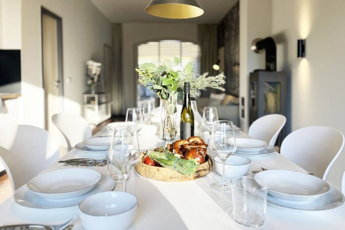 A dining table set with plates, glasses, and a centerpiece of vegetables and bread.
