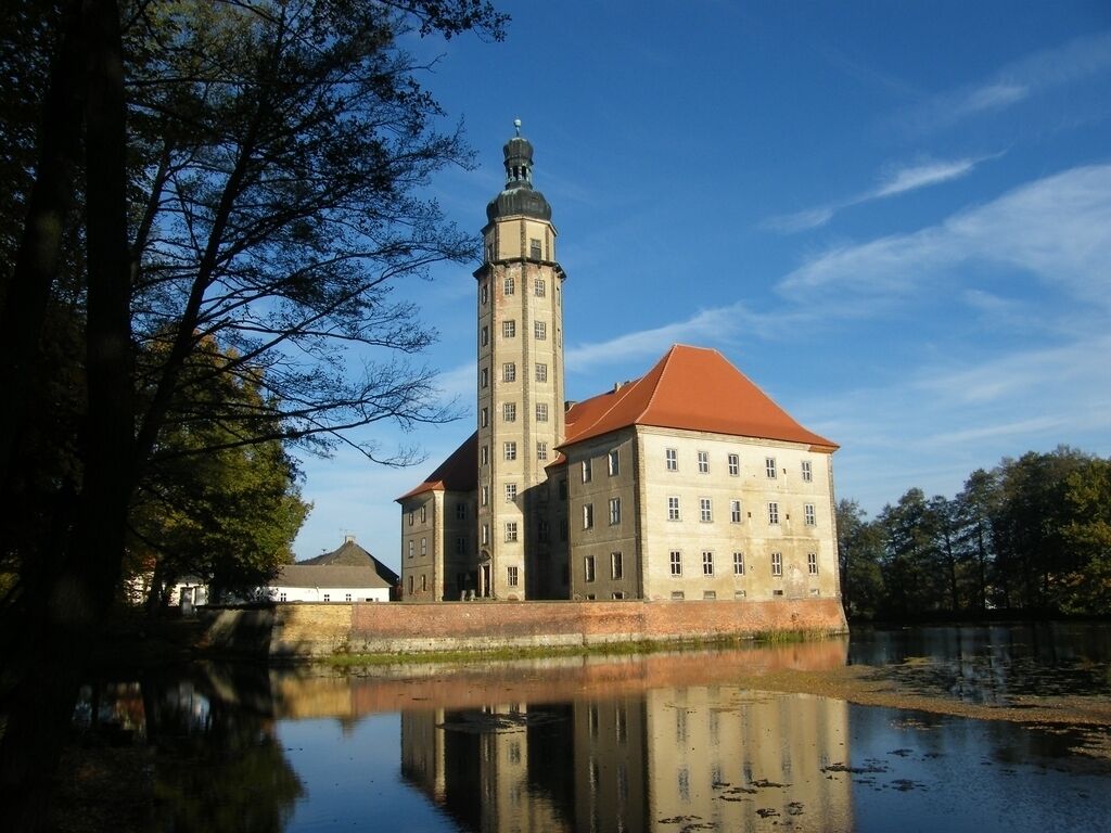 Um edifício histórico com uma torre imponente e um grande edifício com telhado vermelho, localizado às margens de águas calmas.