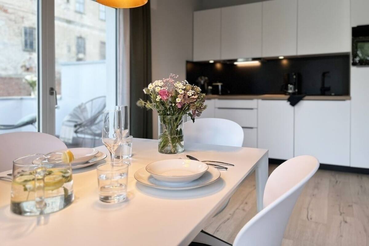 A modern kitchen with white cabinets, a dining table set with plates, glasses, and a vase of flowers.