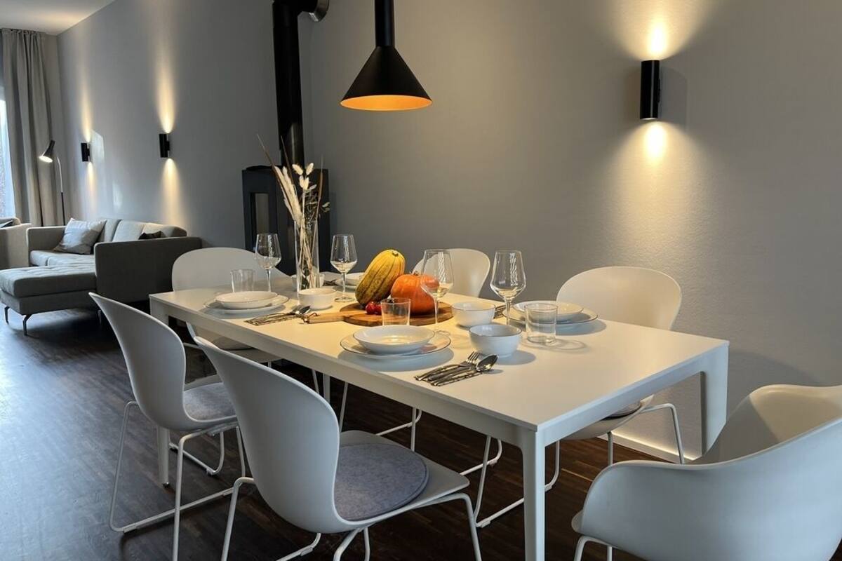 A modern dining area with a white table set for four, surrounded by white chairs.