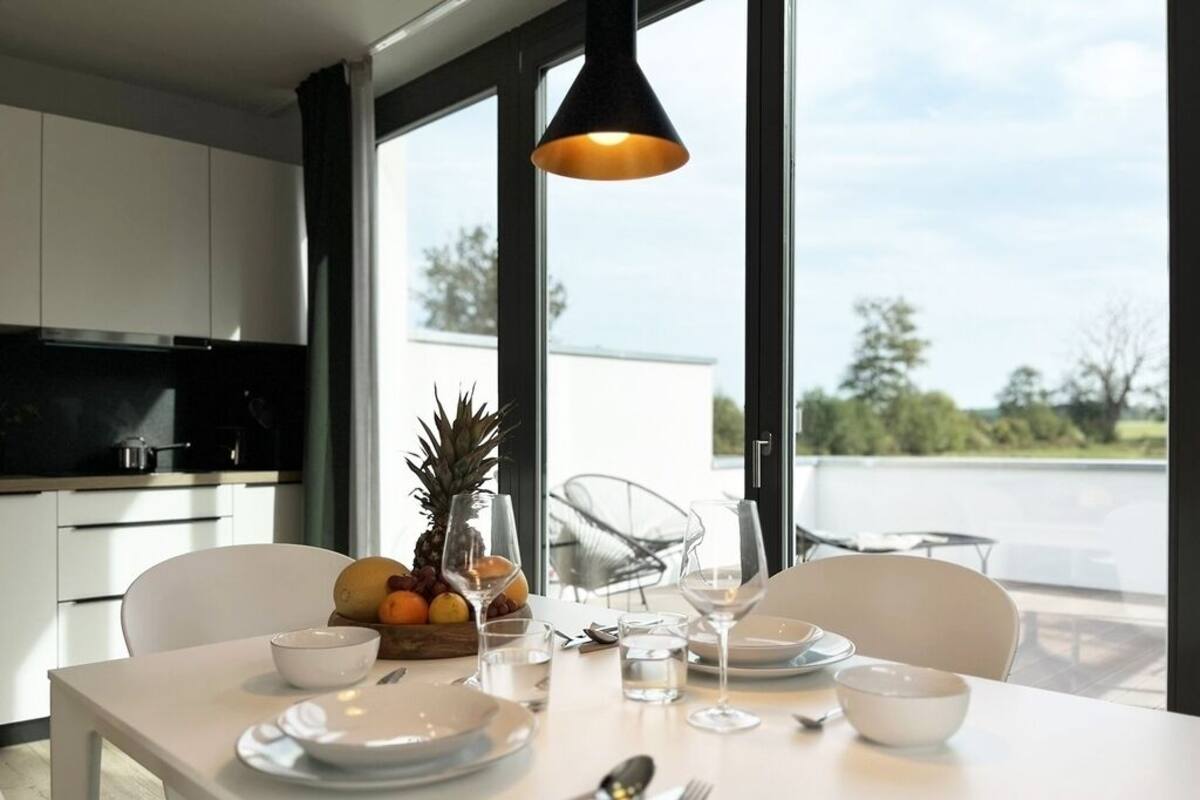 A modern dining area with a table set for two, featuring a fruit bowl, wine glasses, and cutlery.