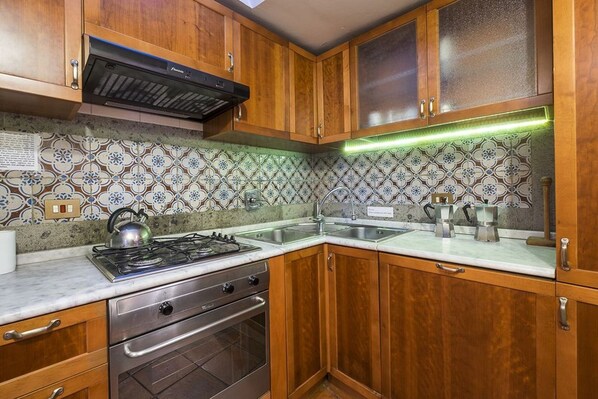 A kitchen with wooden cabinets, a gas stove, an oven, a sink, and a backsplash with a floral pattern. - NAVONA PENTHOUSE APARTMENT WITH TERRACES (Roma)